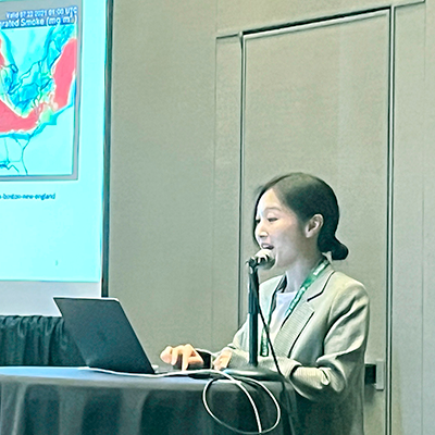 Manzhu Yu standing at a podium presenting research on spatio-temporal methods.