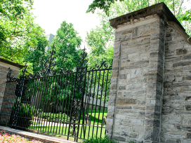 A wrought iron gate and stone wall, with trees in the background