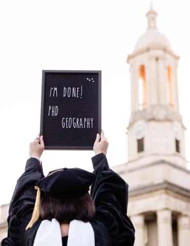 graduate holding a sign that says "I'm done PhD Geography"